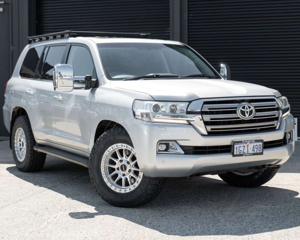 A silver Toyota Land Cruiser 200 series 200series SUV parked outdoors in front of a dark metal garage door at motormall , showing the front and side three-quarter view. DSpeed D-Speed XT xt-1 18x9 wheels +18 offset with 275/70R18 comforser all terrain cf1100 tyres 4x4 offroad wheels and tyres off road rims alloys