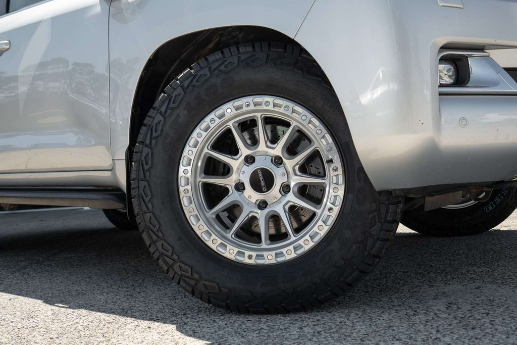 A silver Toyota Land Cruiser 200 series 200series SUV parked outdoors in front of a dark metal garage door at motormall , showing the front and side three-quarter view. DSpeed D-Speed XT xt-1 18x9 wheels +18 offset with 275/70R18 comforser all terrain cf1100 tyres 4x4 offroad wheels and tyres off road rims alloys