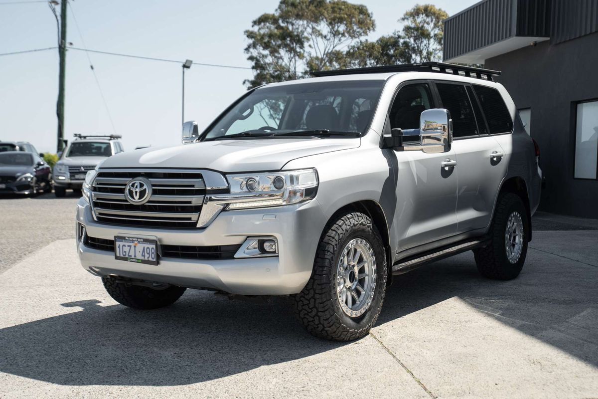 A silver Toyota Land Cruiser 200 series 200series SUV parked outdoors in front of a dark metal garage door at motormall , showing the front and side three-quarter view. DSpeed D-Speed XT xt-1 18x9 wheels +18 offset with 275/70R18 comforser all terrain cf1100 tyres 4x4 offroad wheels and tyres off road rims alloys