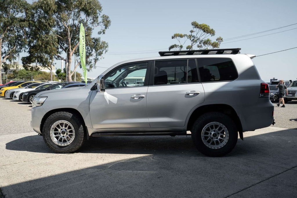 A silver Toyota Land Cruiser 200 series 200series SUV parked outdoors in front of a dark metal garage door at motormall , showing the front and side three-quarter view. DSpeed D-Speed XT xt-1 18x9 wheels +18 offset with 275/70R18 comforser all terrain cf1100 tyres 4x4 offroad wheels and tyres off road rims alloys
