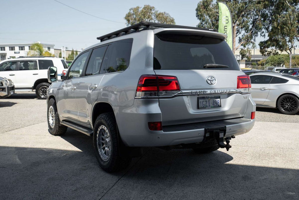 A silver Toyota Land Cruiser 200 series 200series SUV parked outdoors in front of a dark metal garage door at motormall , showing the front and side three-quarter view. DSpeed D-Speed XT xt-1 18x9 wheels +18 offset with 275/70R18 comforser all terrain cf1100 tyres 4x4 offroad wheels and tyres off road rims alloys