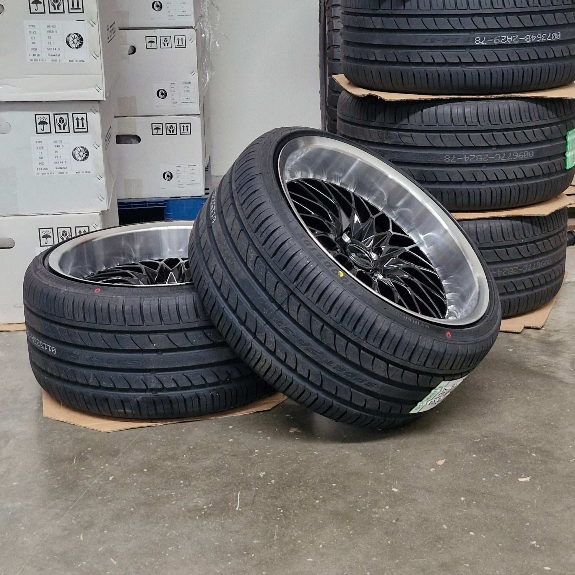 Tires with rims on a concrete floor with boxes in the background