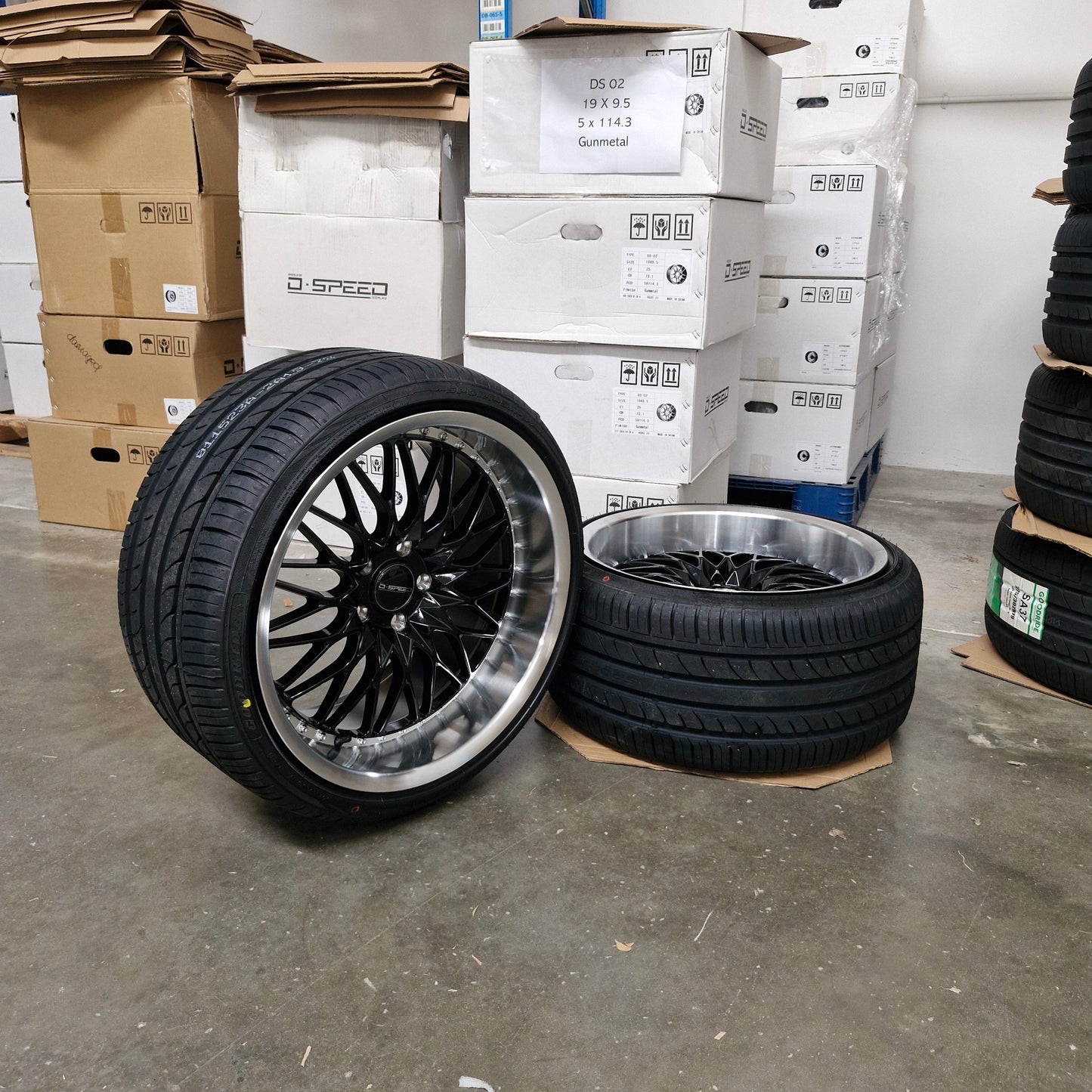 Two car tires with black rims on a concrete floor next to cardboard boxes.