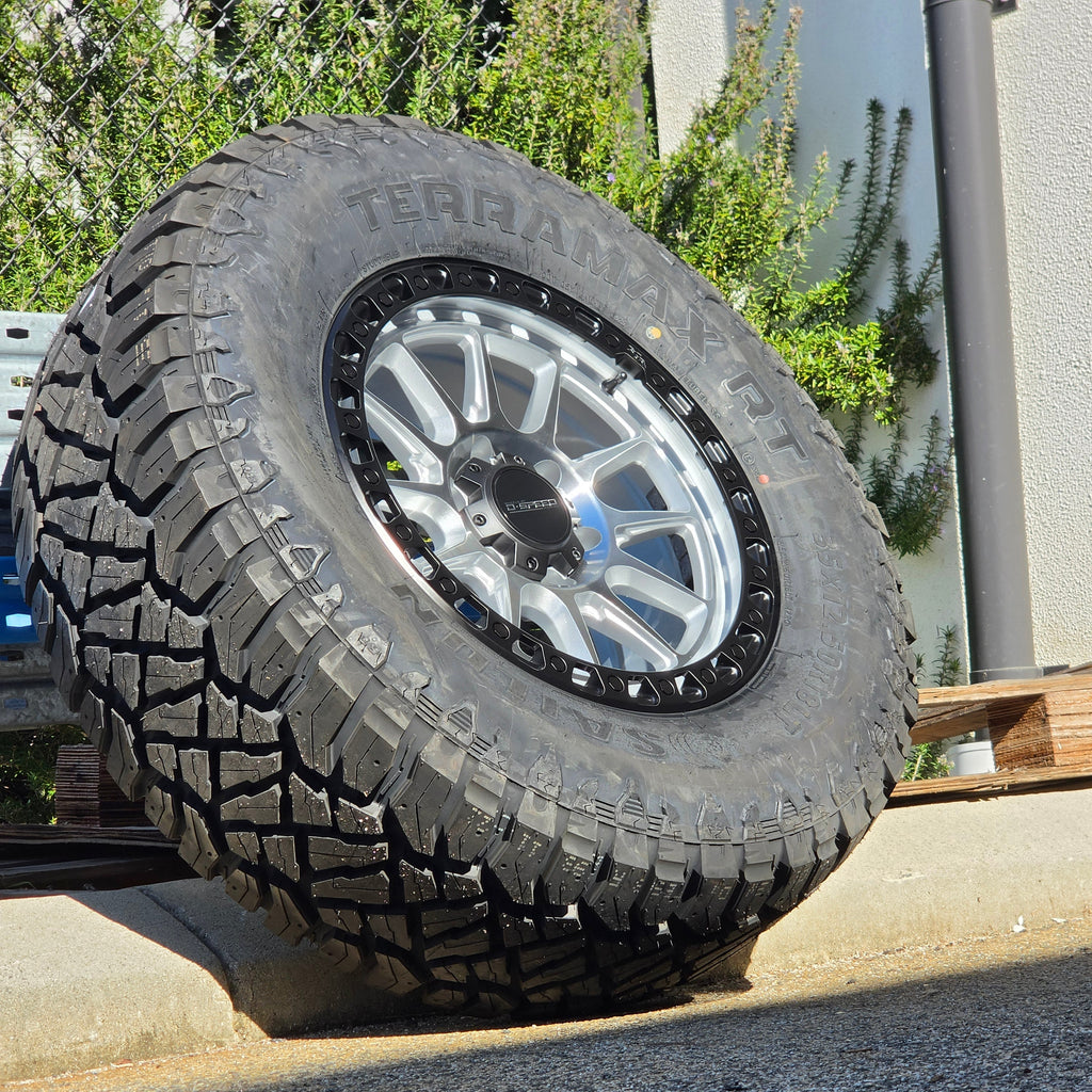 A black off-road tire with visible 'SAILUN terramax RT' lettering, mounted on a multi-spoke silver and black wheel, photographed outdoors against a chain-link fence and blue sky. Dspeed xt-1 xt1 wheel silver with black ring 17x9 17x8.5 18x9 4x4 offroad wheels rims