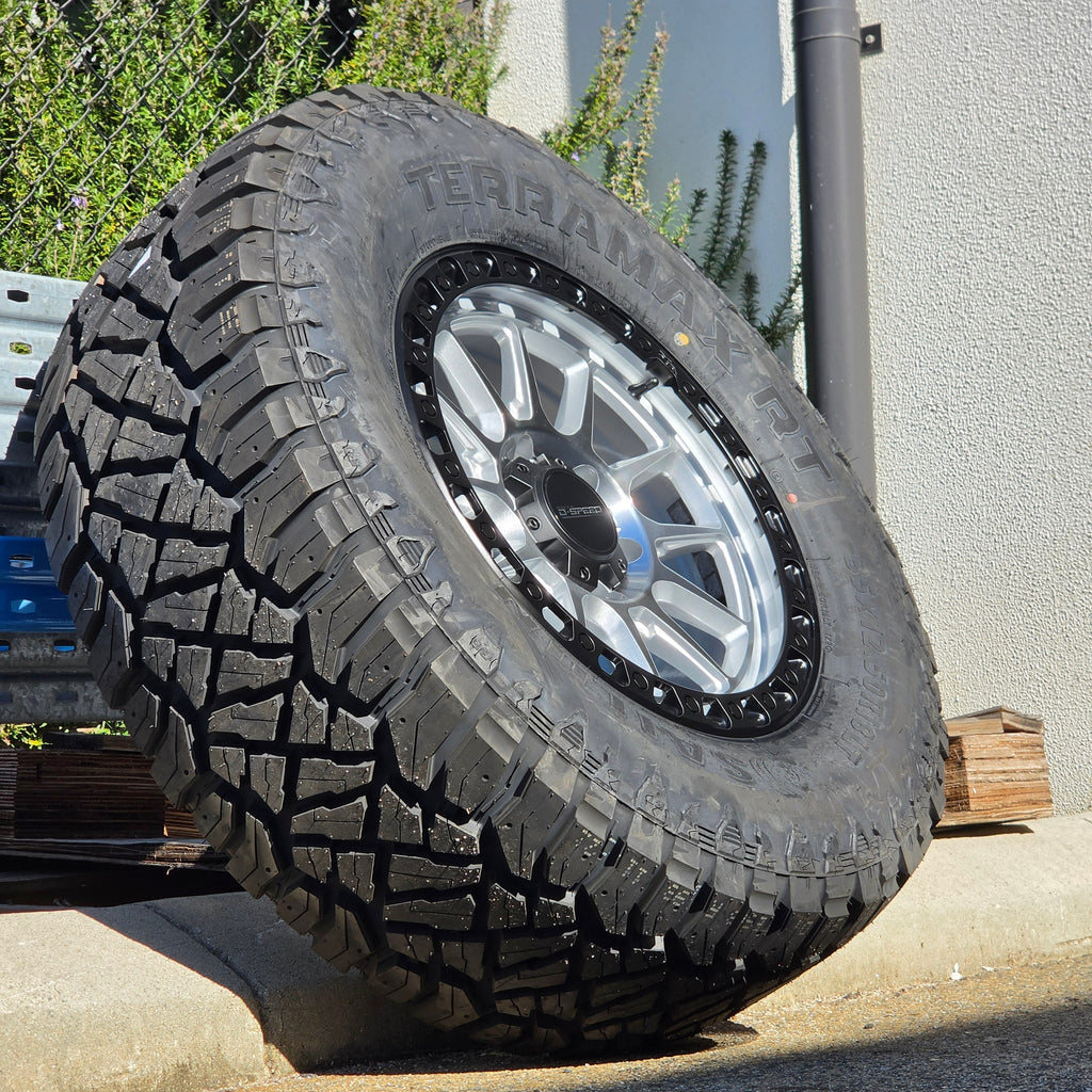 A black off-road tire with visible 'SAILUN terramax RT' lettering, mounted on a multi-spoke silver and black wheel, photographed outdoors against a chain-link fence and blue sky. Dspeed xt-1 xt1 wheel silver with black ring 17x9 17x8.5 18x9 4x4 offroad wheels rims