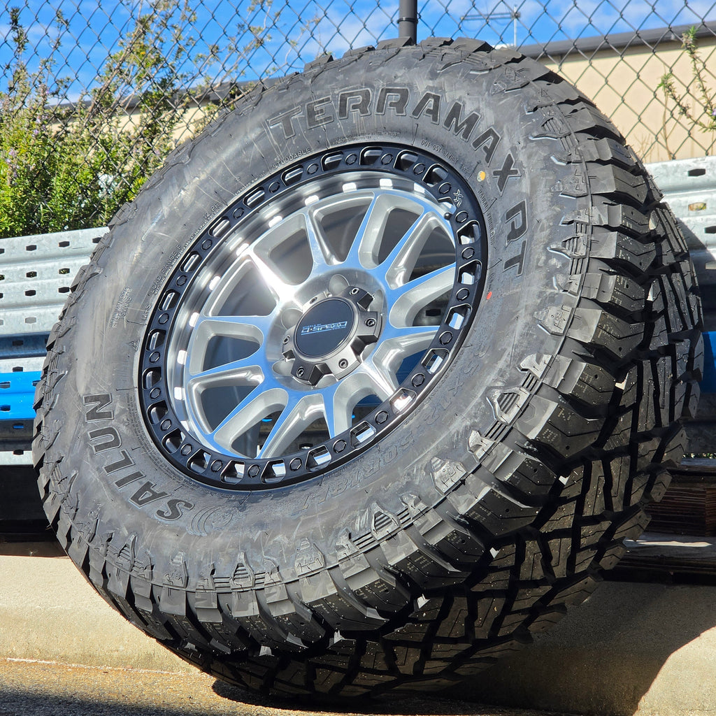 A black off-road tire with visible 'SAILUN terramax RT' lettering, mounted on a multi-spoke silver and black wheel, photographed outdoors against a chain-link fence and blue sky. Dspeed xt-1 xt1 wheel silver with black ring 17x9 17x8.5 18x9 4x4 offroad wheels rims