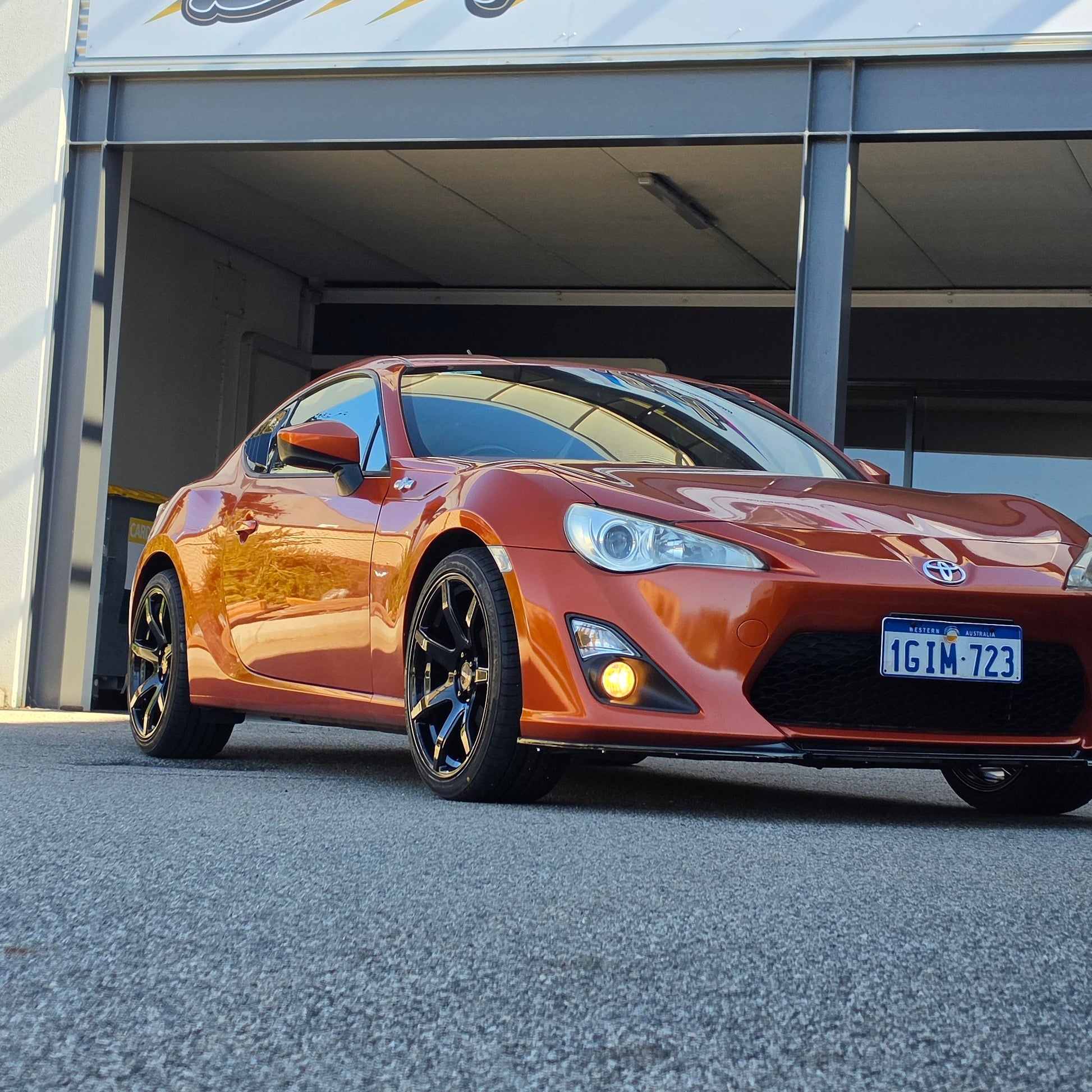 A metallic copper orange sports car parked inside a garage bay, with a large vertical banner reading 'd Speed ' hanging beside the open DSpeed DS-07 ds07 18x8.5 +35 5x100 alloy wheels rims concave gloss black