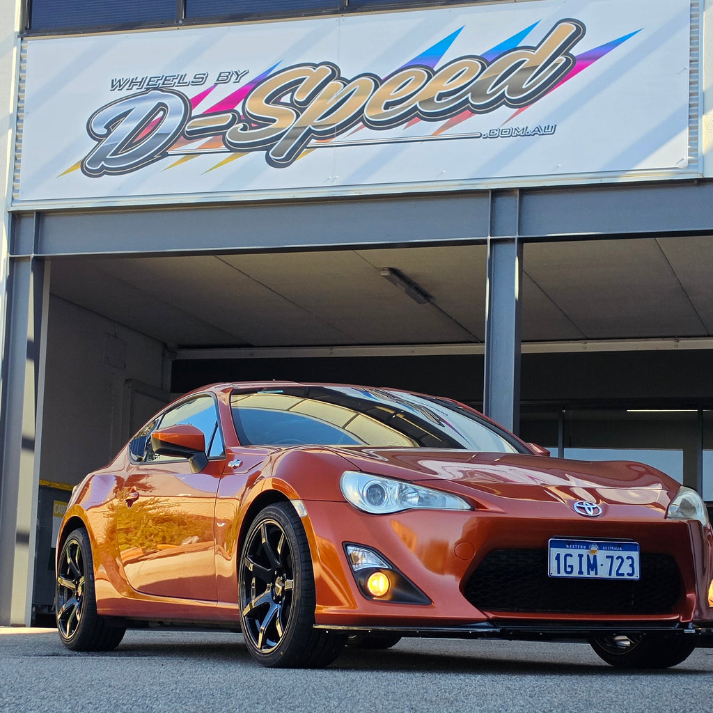 A metallic copper orange sports car parked inside a garage bay, with a large vertical banner reading 'd Speed ' hanging beside the open DSpeed DS-07 ds07 18x8.5 +35 5x100 alloy wheels rims concave gloss black