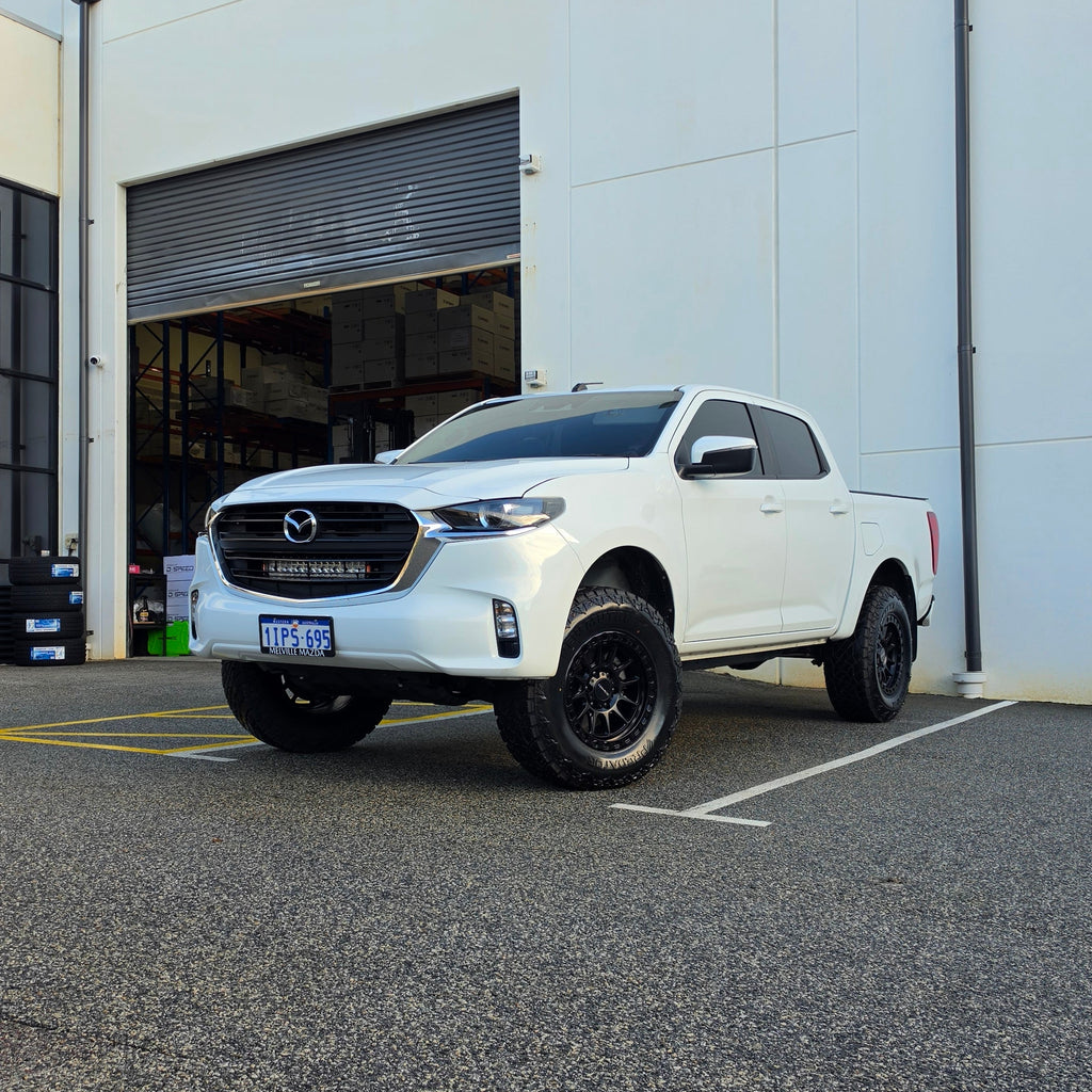 A white Mazda bt50 bt-50 pickup truck parked on asphalt in front of a dspeed d-speed industrial building with a garage door. xt-1 wheel 4x4 rims 285 tyres 285/70r17 at xt rt mt all terrain