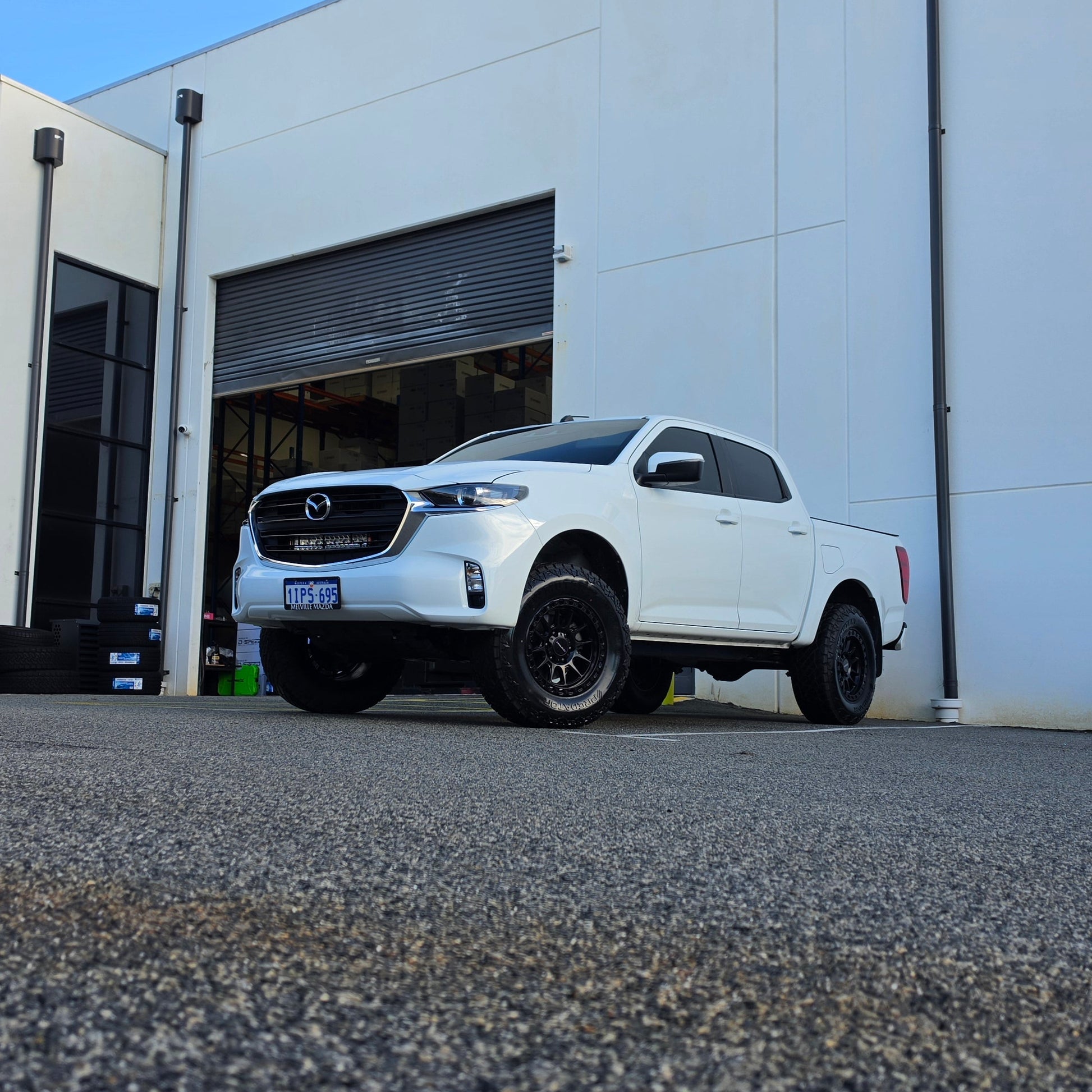 A white Mazda bt50 bt-50 pickup truck parked on asphalt in front of a dspeed d-speed industrial building with a garage door. xt-1 wheel 4x4 rims 285 tyres 285/70r17 at xt rt mt all terrain