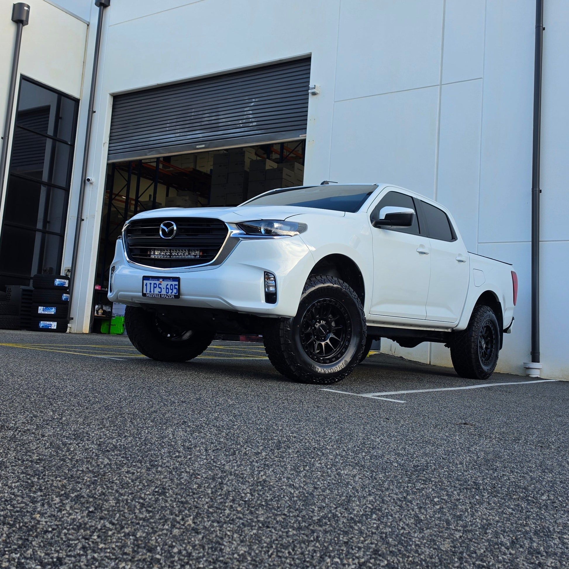 A white Mazda bt50 bt-50 pickup truck parked on asphalt in front of a dspeed d-speed industrial building with a garage door. xt-1 wheel 4x4 rims 285 tyres 285/70r17 at xt rt mt all terrain