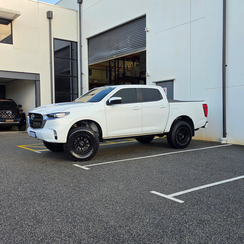 A white Mazda bt50 bt-50 pickup truck parked on asphalt in front of a dspeed d-speed industrial building with a garage door. xt-1 wheel 4x4 rims 285 tyres 285/70r17 at xt rt mt all terrain