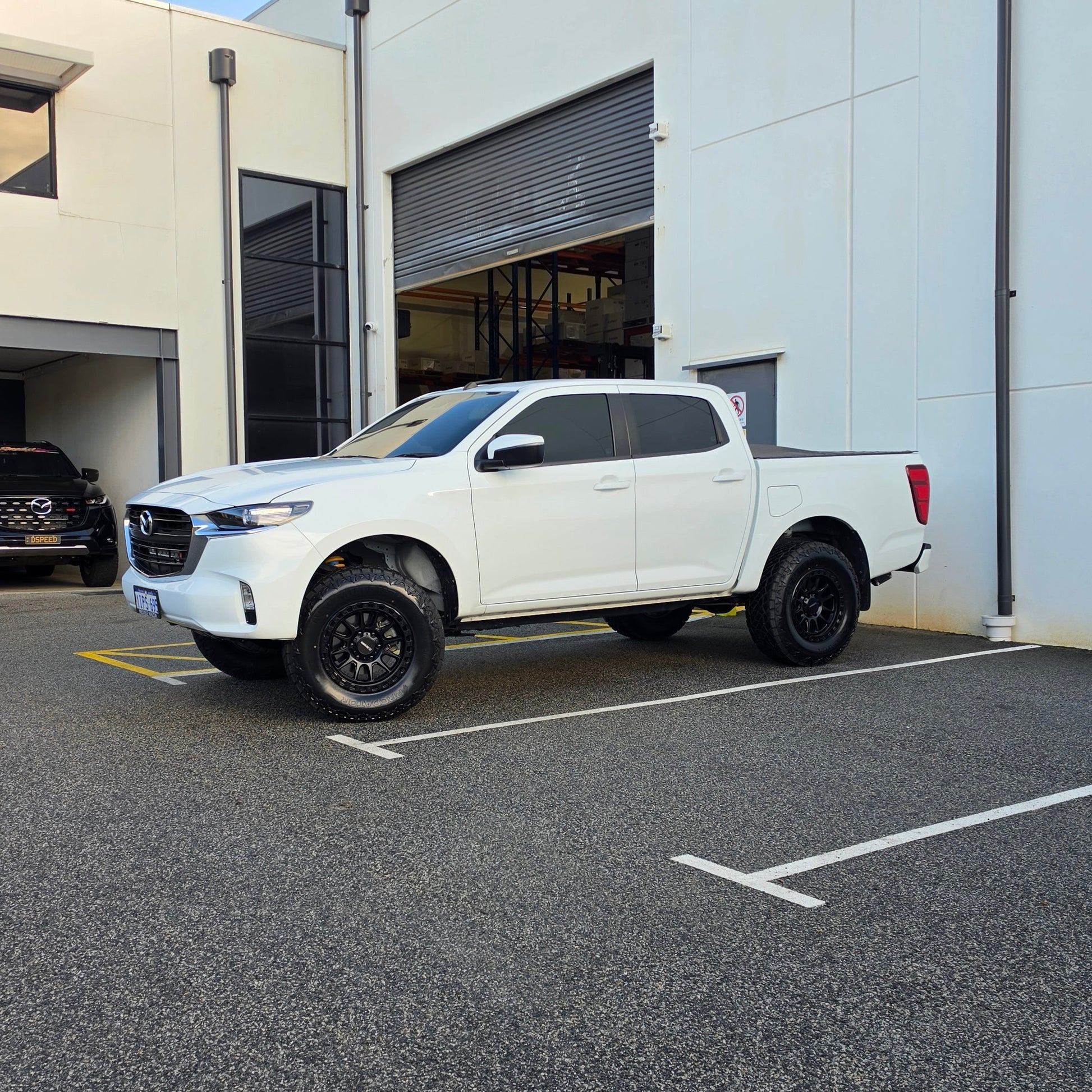 A white Mazda bt50 bt-50 pickup truck parked on asphalt in front of a dspeed d-speed industrial building with a garage door. xt-1 wheel 4x4 rims 285 tyres 285/70r17 at xt rt mt all terrain