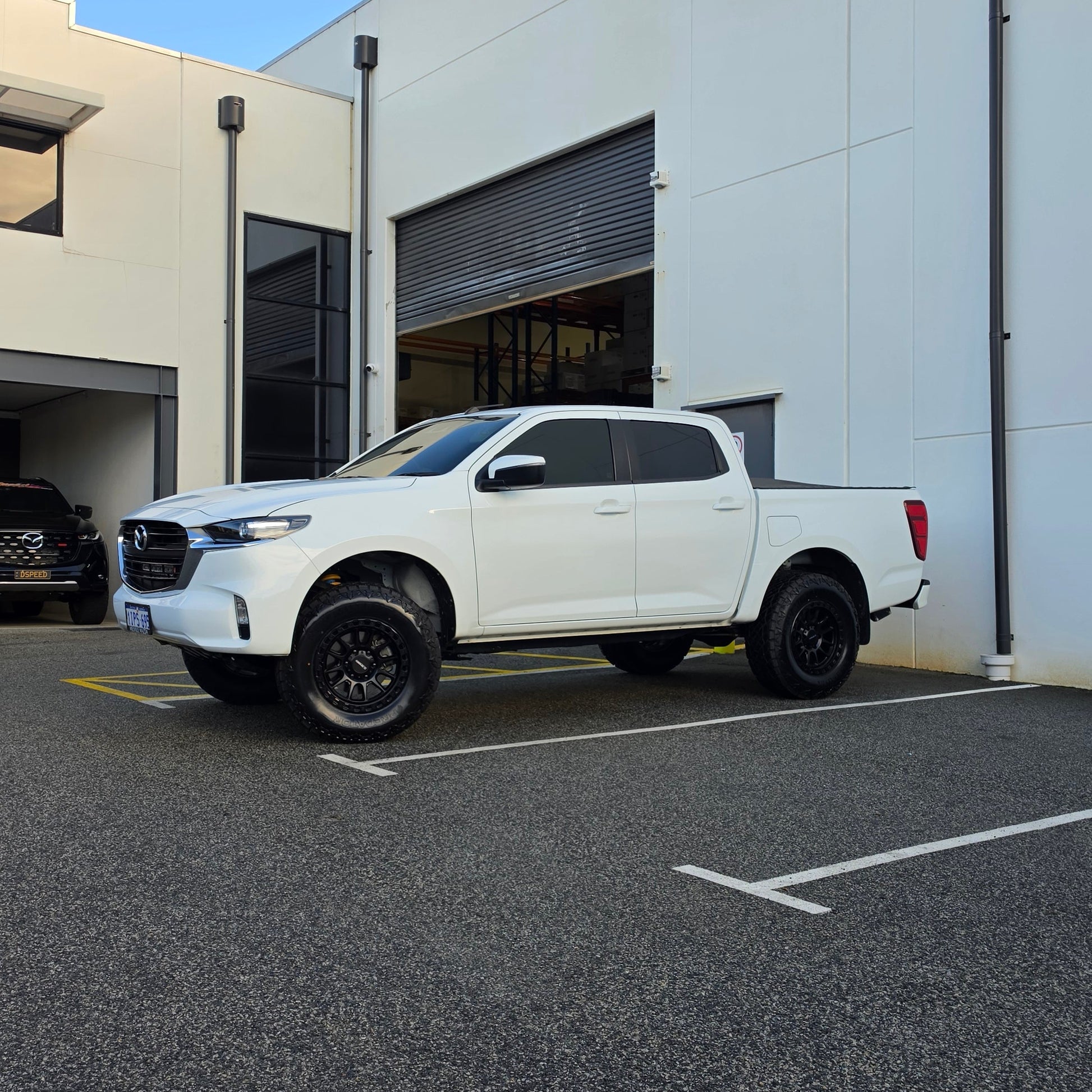 A white Mazda bt50 bt-50 pickup truck parked on asphalt in front of a dspeed d-speed industrial building with a garage door. xt-1 wheel 4x4 rims 285 tyres 285/70r17 at xt rt mt all terrain