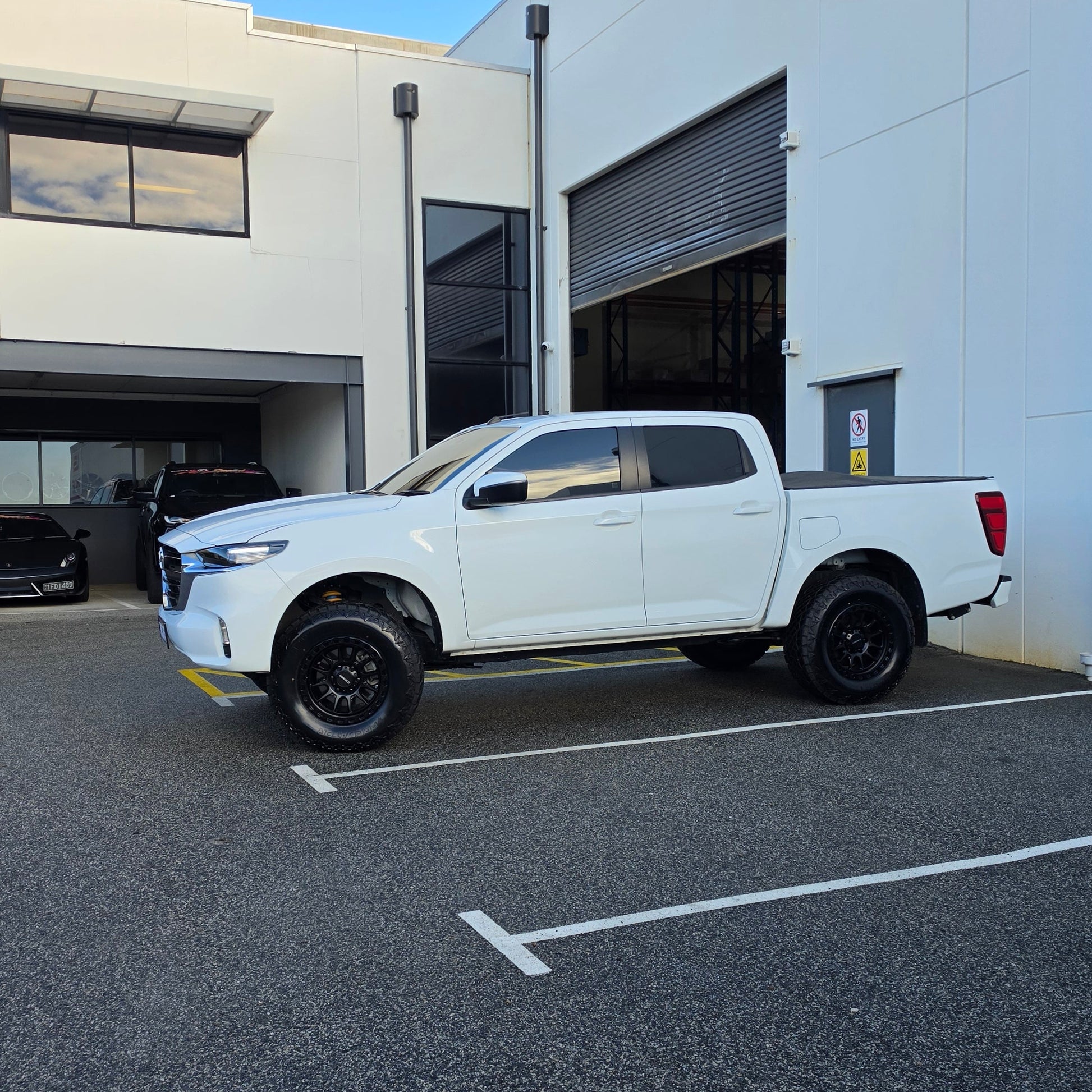 A white Mazda bt50 bt-50 pickup truck parked on asphalt in front of a dspeed d-speed industrial building with a garage door. xt-1 wheel 4x4 rims 285 tyres 285/70r17 at xt rt mt all terrain