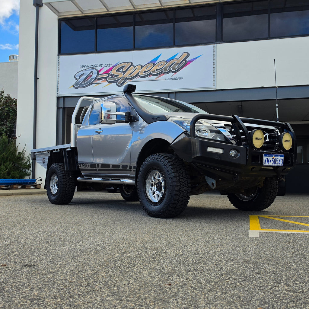 A silver lifted pickup truck with a black bull bar and off-road tires parked in front of a building with a d-speed sign. dspeed mh1 mh-1 alloy wheels 4x4 rims and comforser tyres 17x8.5 machined silver black ring