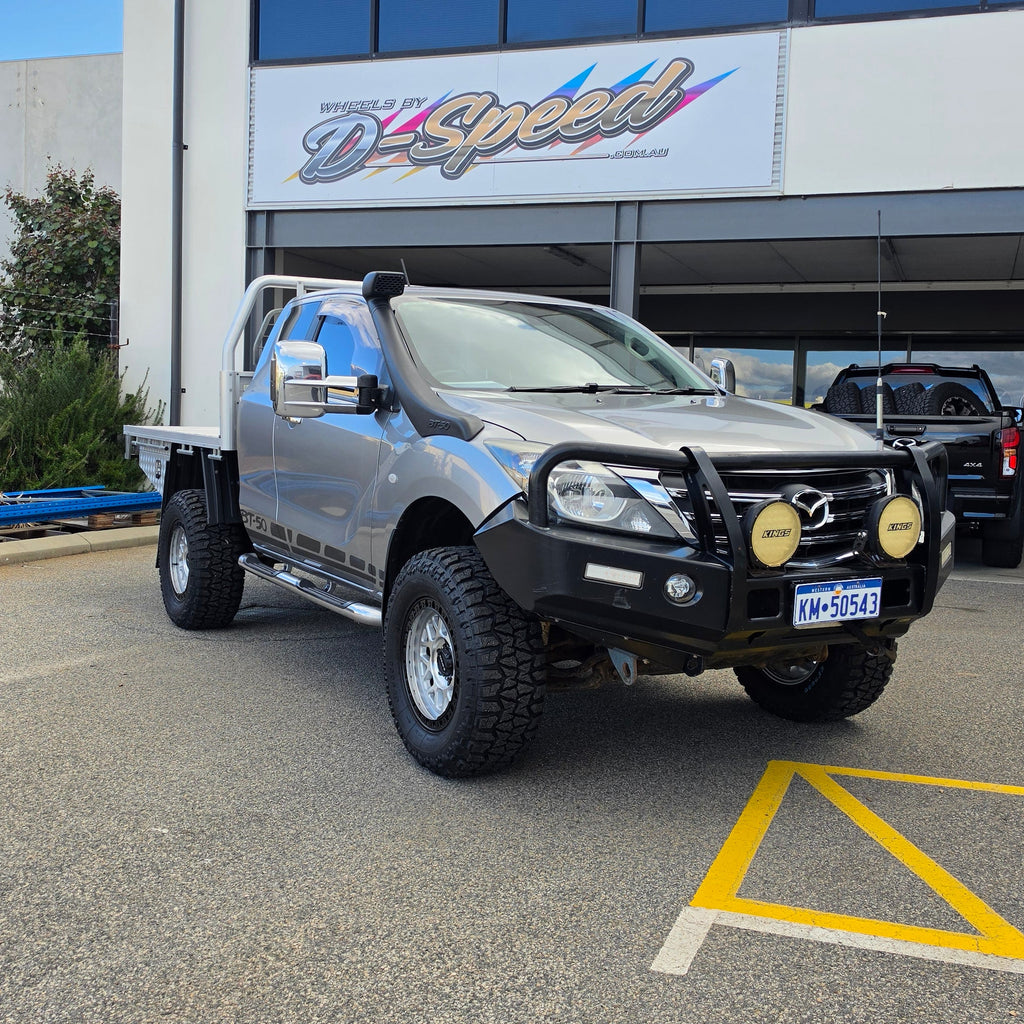 A silver lifted pickup truck with a black bull bar and off-road tires parked in front of a building with a d-speed sign. dspeed mh1 mh-1 alloy wheels 4x4 rims and comforser tyres 17x8.5 machined silver black ring