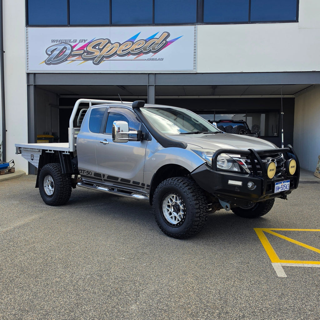 A silver lifted pickup truck with a black bull bar and off-road tires parked in front of a building with a d-speed sign. dspeed mh1 mh-1 alloy wheels 4x4 rims and comforser tyres 17x8.5 machined silver black ring