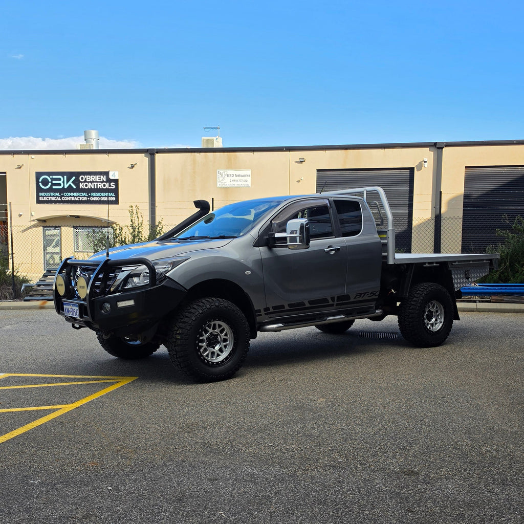 A dark gray off-road BT-50 with DSpeed MH-1 D-Speed MH1 4x4 off road offroad wheels 17x8.5 machined silver black Ring custom flatbed and front bumper guard parked in a paved lot in front of a beige commercial building under a blue sky.