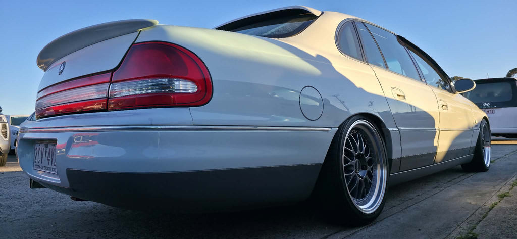 A white holden Statesman parked outdoors on a gravel lot, featuring a lowered suspension, custom multi-spoke alloy wheels, and a tinted rear window. Dspeed d-speed ds06 ds-06 19inch 19x8.5 19x9.5 wheels with tyres dish wheels dished rims