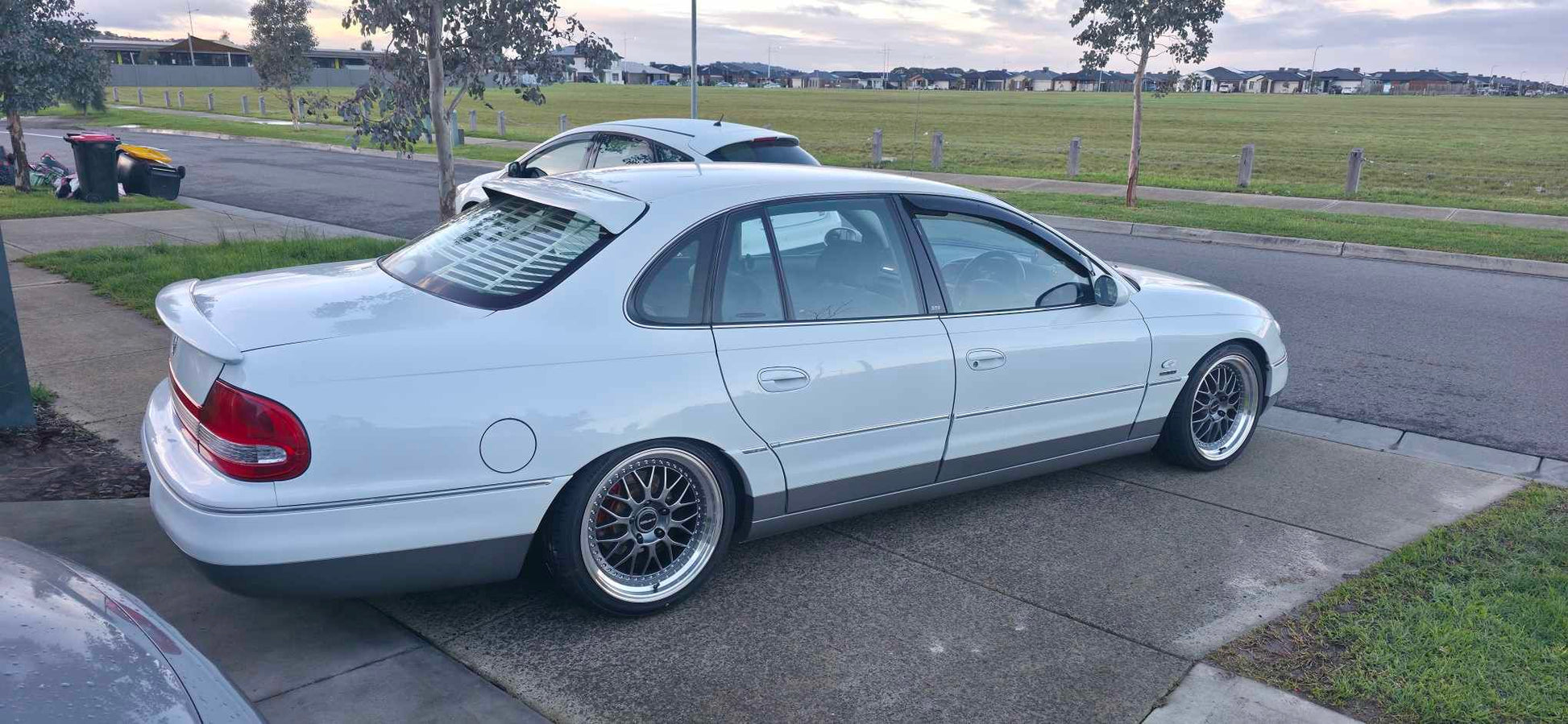 A white holden Statesman parked outdoors on a gravel lot, featuring a lowered suspension, custom multi-spoke alloy wheels, and a tinted rear window. Dspeed d-speed ds06 ds-06 19inch 19x8.5 19x9.5 wheels with tyres dish wheels dished rims