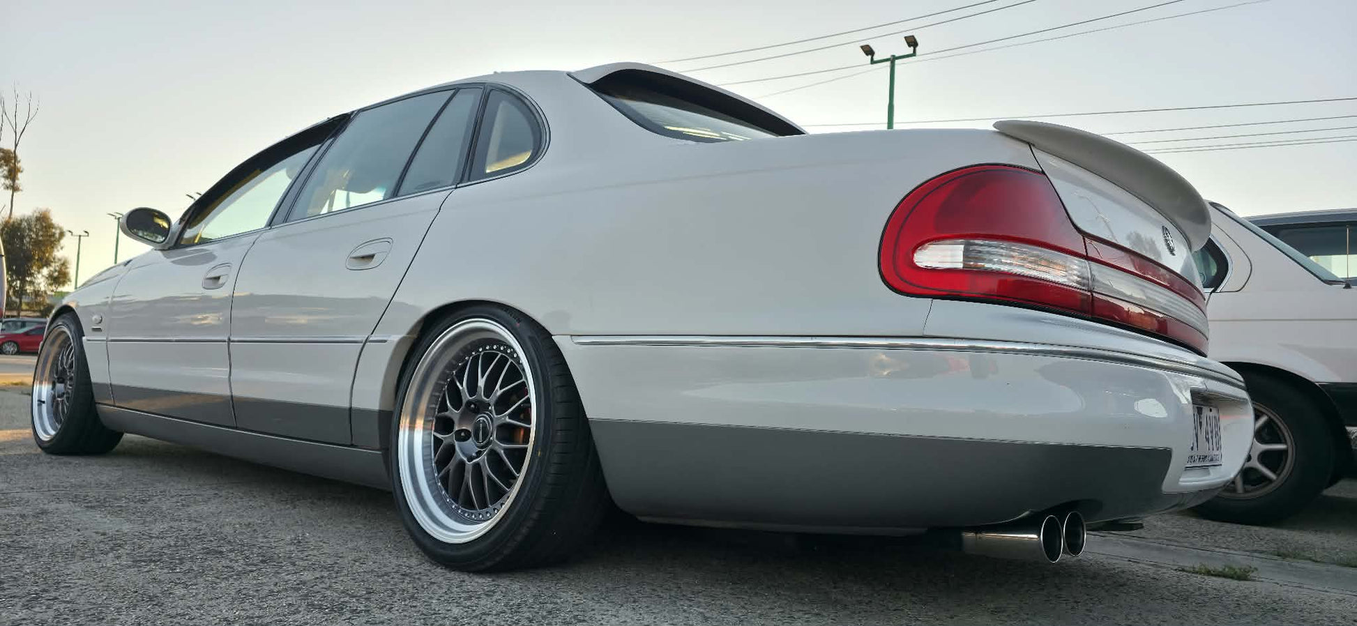 A white holden Statesman parked outdoors on a gravel lot, featuring a lowered suspension, custom multi-spoke alloy wheels, and a tinted rear window. Dspeed d-speed ds06 ds-06 19inch 19x8.5 19x9.5 wheels with tyres dish wheels dished rims