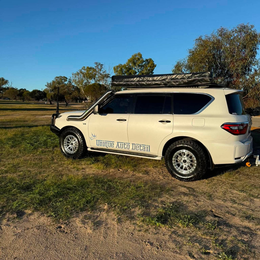 A white nissan patrol Y62 off-road SUV parked outdoors on grassy ground under a blue sky, with a black roof rack, front bull bar, and off-road tires. DSpeed d-speed XT-1 xt1 18x9 wheels 4x4 rims off road offroad