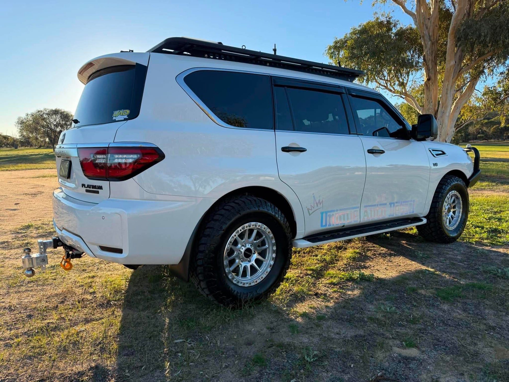 A white nissan patrol Y62 off-road SUV parked outdoors on grassy ground under a blue sky, with a black roof rack, front bull bar, and off-road tires. DSpeed d-speed XT-1 xt1 18x9 wheels 4x4 rims off road offroad
