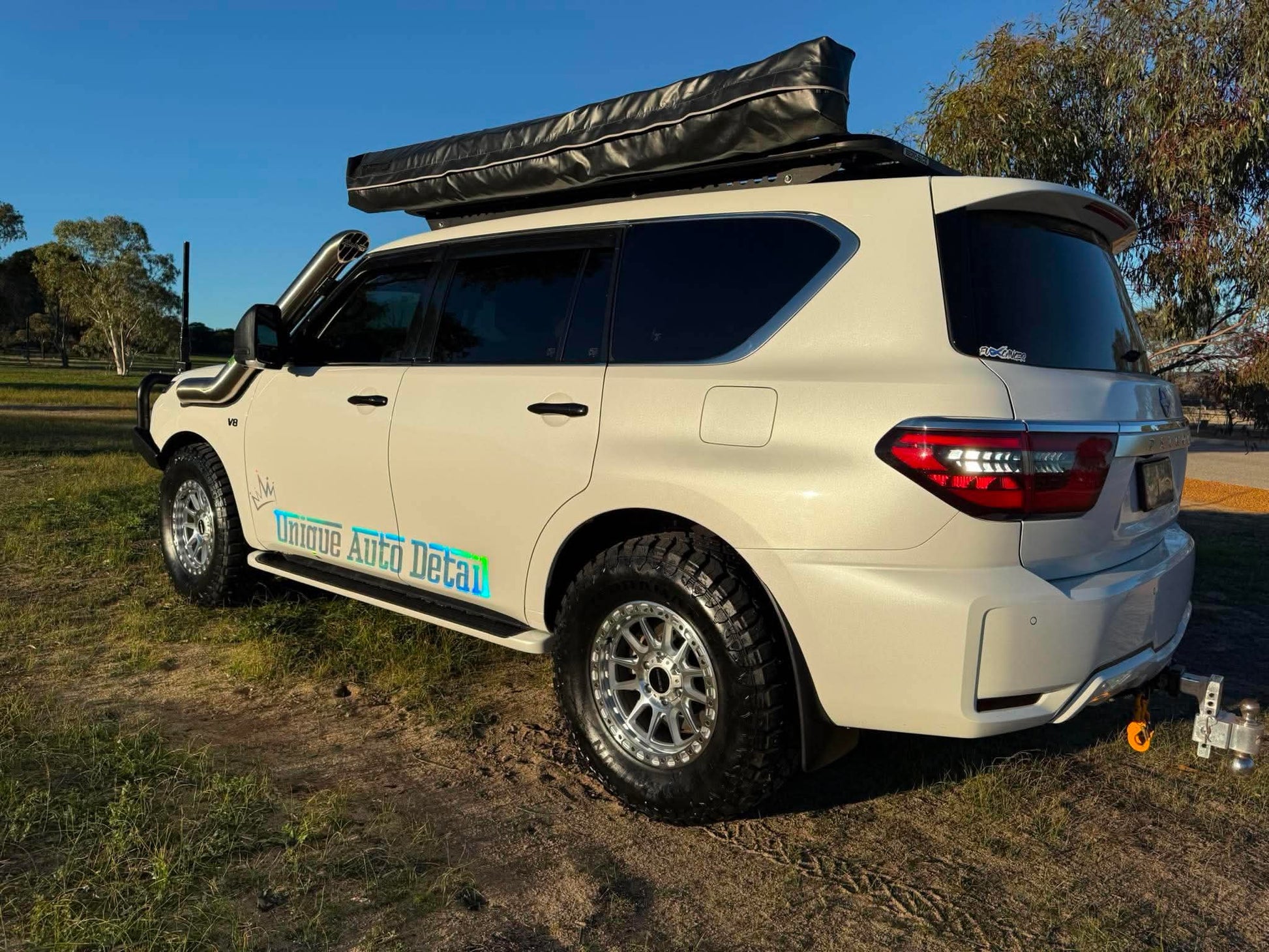 A white nissan patrol Y62 off-road SUV parked outdoors on grassy ground under a blue sky, with a black roof rack, front bull bar, and off-road tires. DSpeed d-speed XT-1 xt1 18x9 wheels 4x4 rims off road offroad
