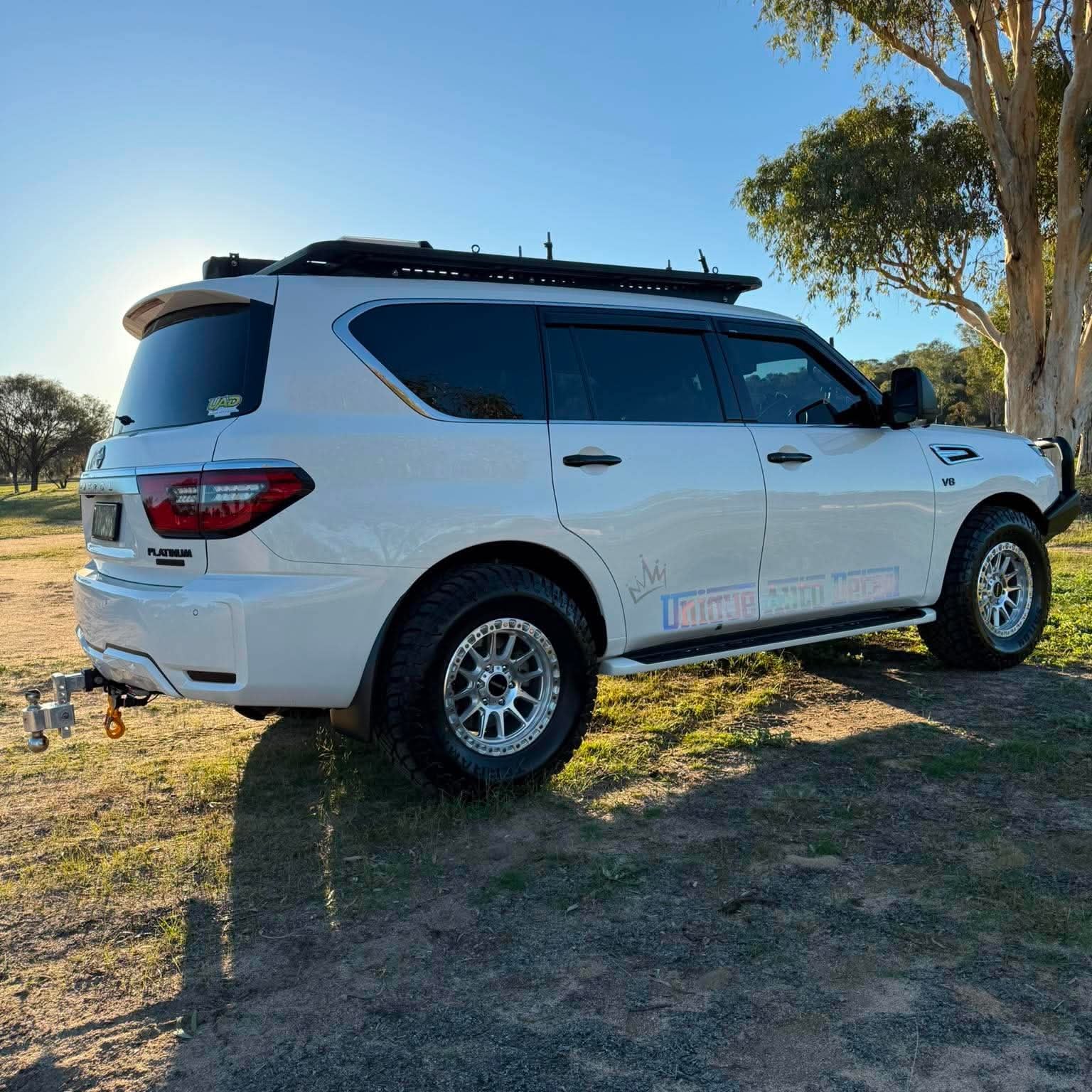 A white nissan patrol Y62 off-road SUV parked outdoors on grassy ground under a blue sky, with a black roof rack, front bull bar, and off-road tires. DSpeed d-speed XT-1 xt1 18x9 wheels 4x4 rims off road offroad