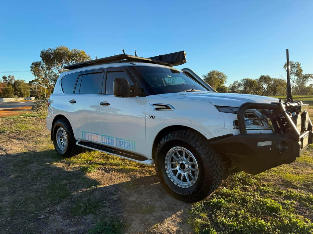 A white nissan patrol Y62 off-road SUV parked outdoors on grassy ground under a blue sky, with a black roof rack, front bull bar, and off-road tires. DSpeed d-speed XT-1 xt1 18x9 wheels 4x4 rims off road offroad