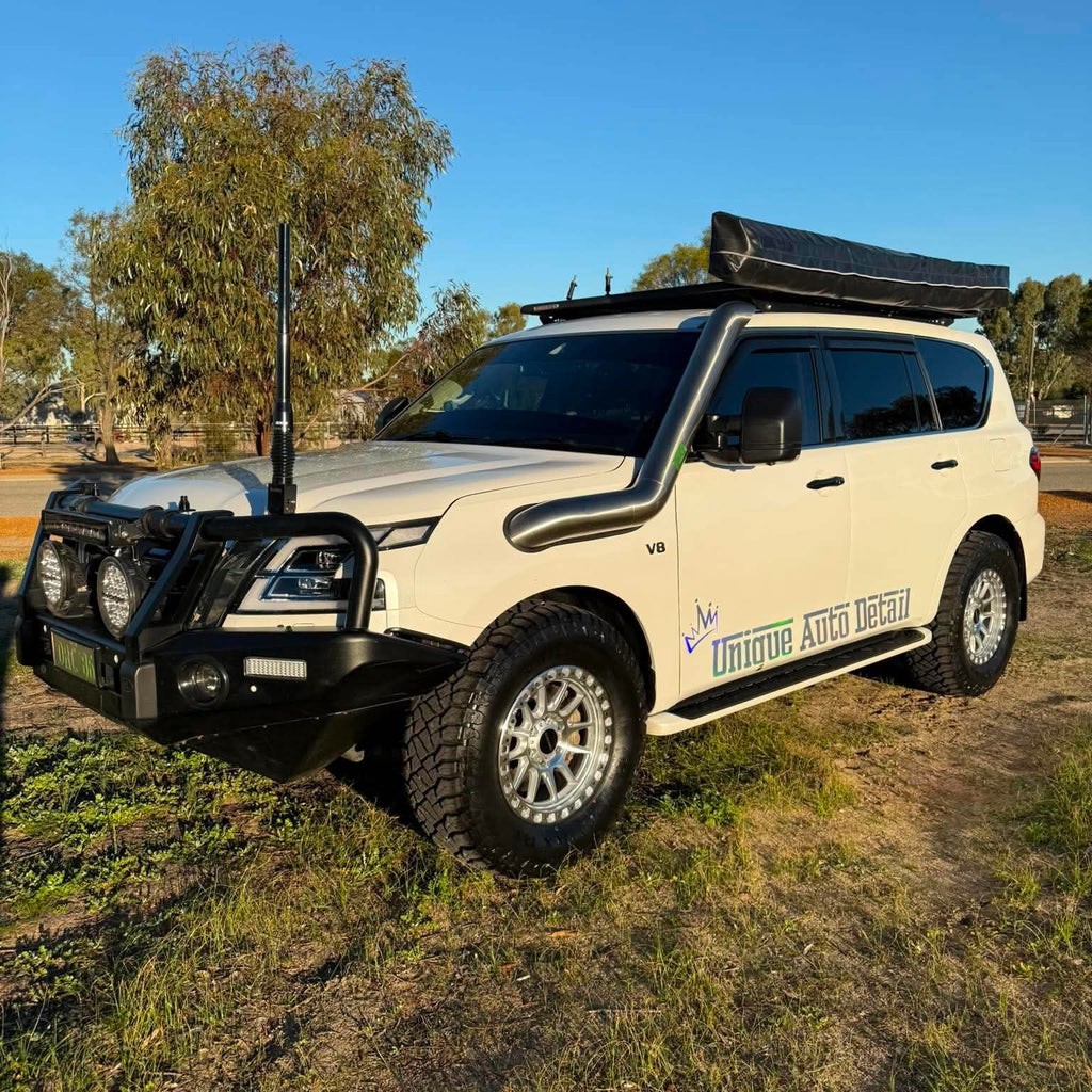 A white nissan patrol Y62 off-road SUV parked outdoors on grassy ground under a blue sky, with a black roof rack, front bull bar, and off-road tires. DSpeed d-speed XT-1 xt1 18x9 wheels 4x4 rims off road offroad